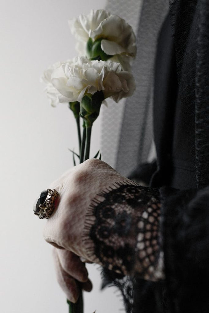 Artistic close-up of a hand holding white carnations, symbolizing elegance and loss.